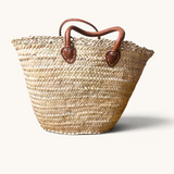 TUYYA handcrafted Moroccan palm leaf wicker basket with camel leather handles and intricate lace-like top detailing.