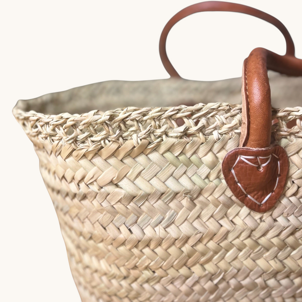 TUYYA handcrafted Moroccan palm leaf wicker basket with camel leather handles and intricate lace-like top detailing.