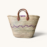 TUYYA Heydi handcrafted Moroccan wicker basket with purple and pink wavy geometric patterns and brown leather handles.