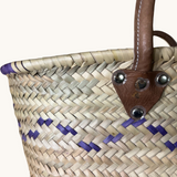 TUYYA Mimmi Moroccan wicker basket with purple wave patterns and brown leather handles secured by metallic rivets.