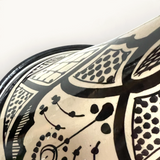 Gros plan sur un tajine en céramique TUYYA noir et blanc avec des motifs floraux marocains peints à la main.