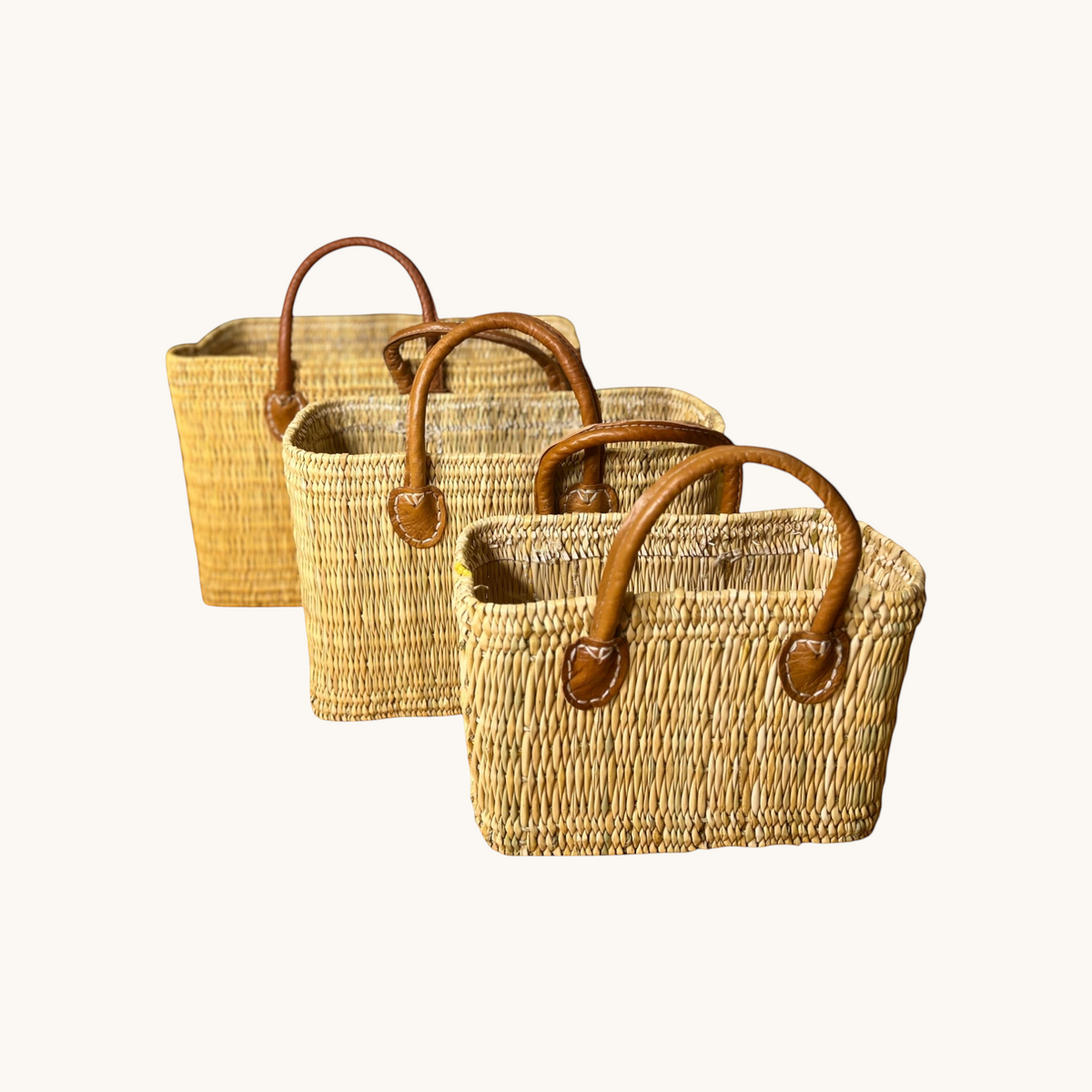 Three tuyya Yasmine structured wicker baskets in different sizes with camel leather handles and rivet details.